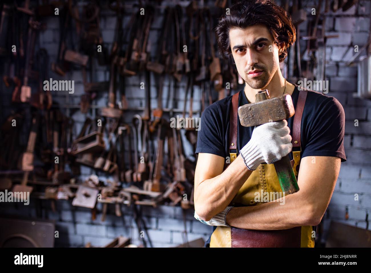 L'autentico uomo fabbro forgia un prodotto in metallo in uno studio interno scuro Foto Stock