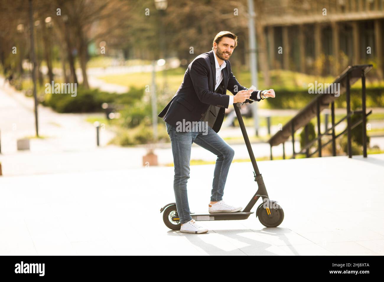 Bel giovane uomo d'affari che usa il telefono cellulare su scooter elettrico Foto Stock