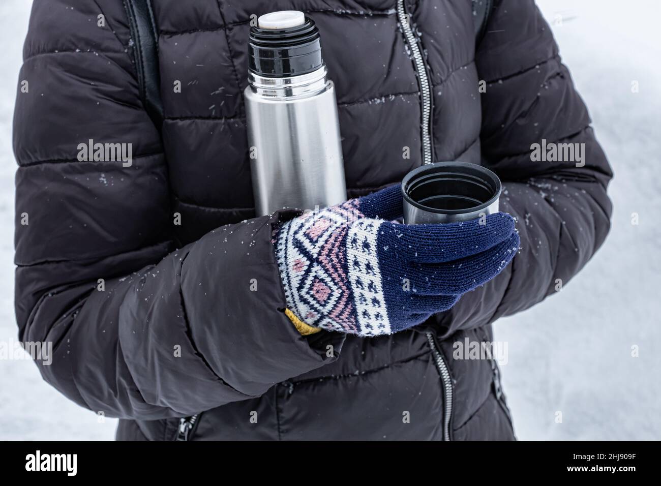 donna che tiene un bicchiere di tè versato da un thermos in inverno sulla strada. Foto di alta qualità Foto Stock