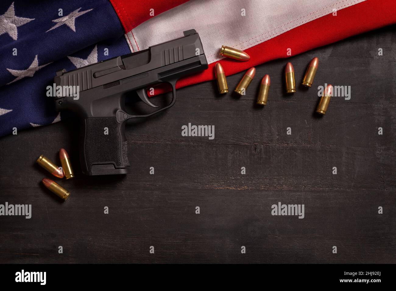 Pistola nera e pallottole con bandiera americana su sfondo dipinto di legno nero Foto Stock