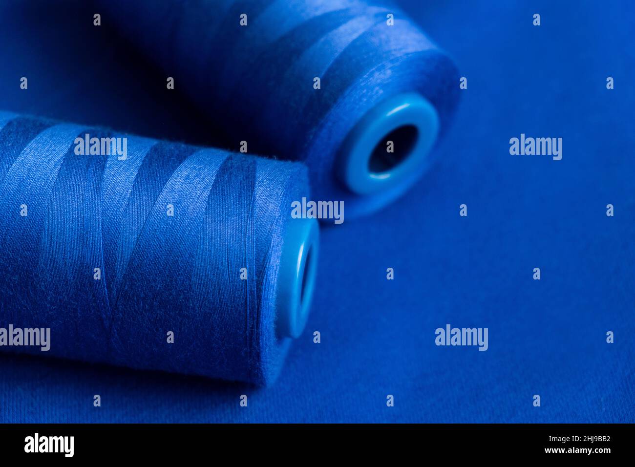 tessuto di filo blu in rocchetto per cucire su fondo blu liscio. primo piano. abbigliamento cucire materiale modello Foto Stock