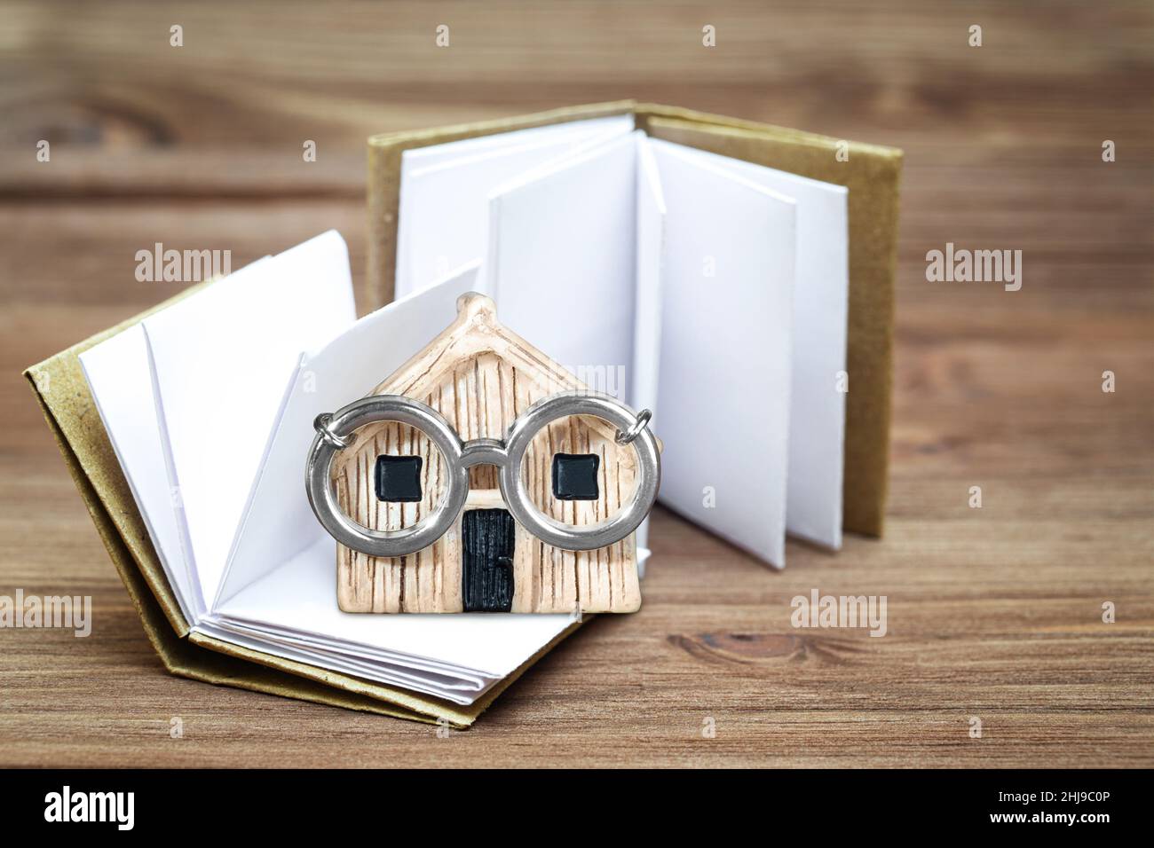 Piccoli libri e un carattere di casa in miniatura indossando occhiali in acciaio su uno sfondo tavolo di legno. Concetto di casa intelligente. Foto Stock