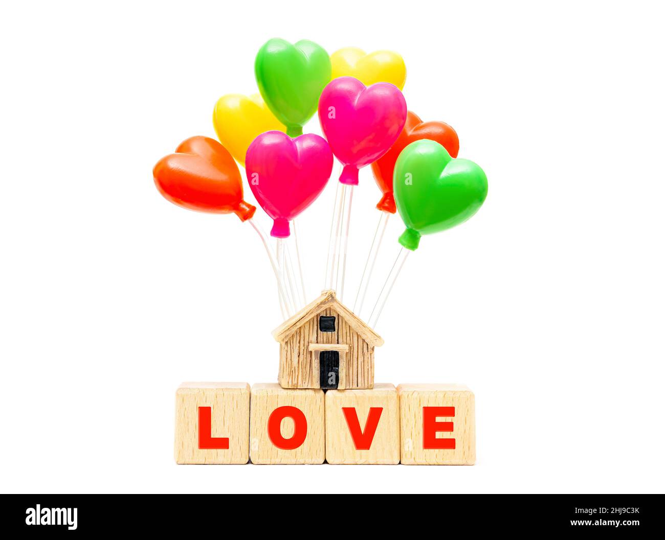 Parola AMORE fatto da blocchi di lettere di legno e un modello di casa in miniatura con palloncini giocattolo a forma di cuore isolato su sfondo bianco. Concetto di Homefullness Foto Stock