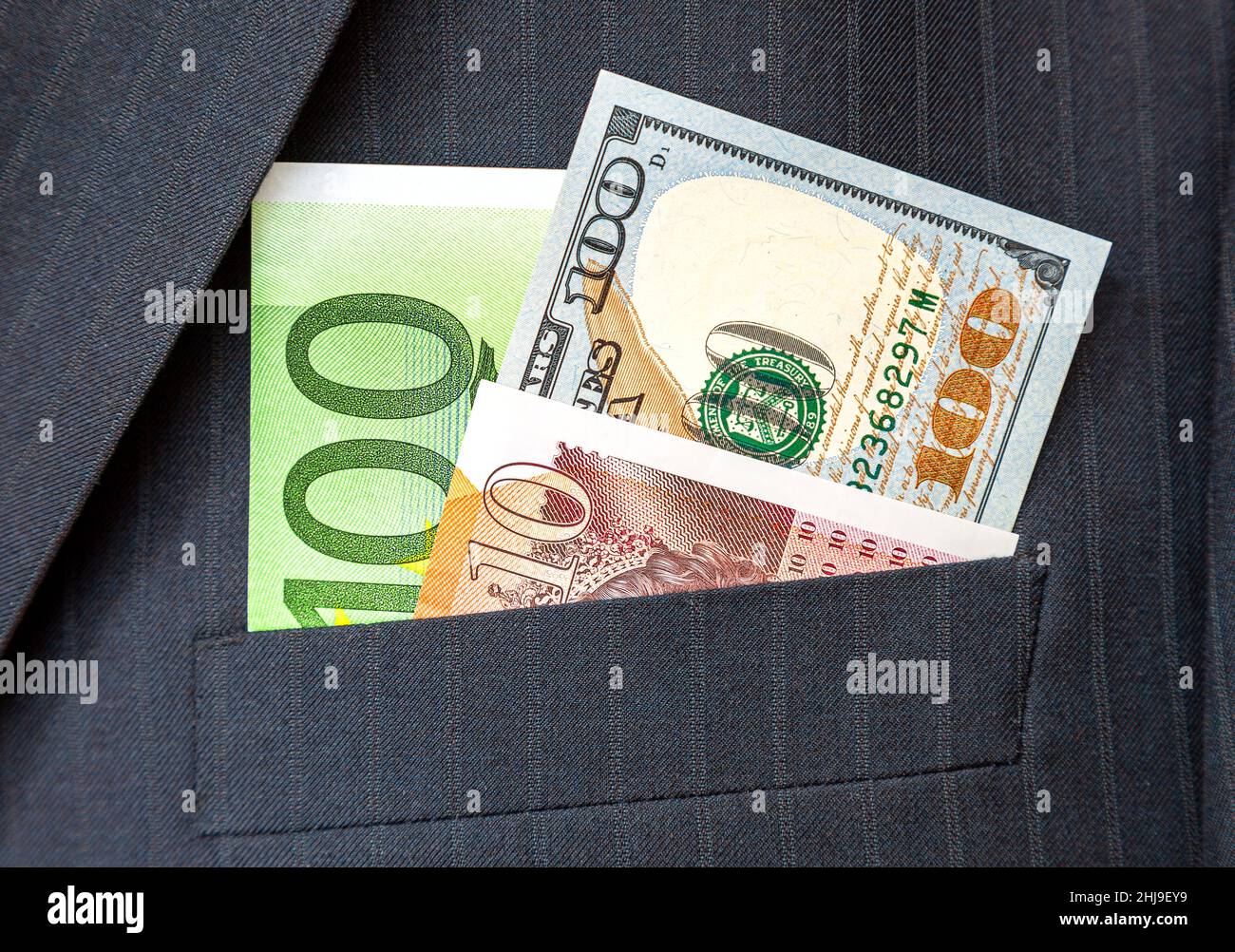 Dollari americani, banconote in euro e sterline britanniche che si stacca fuori dalla tasca del vestito dell'uomo d'affari. Soldi in tasca del vestito di affari Foto Stock
