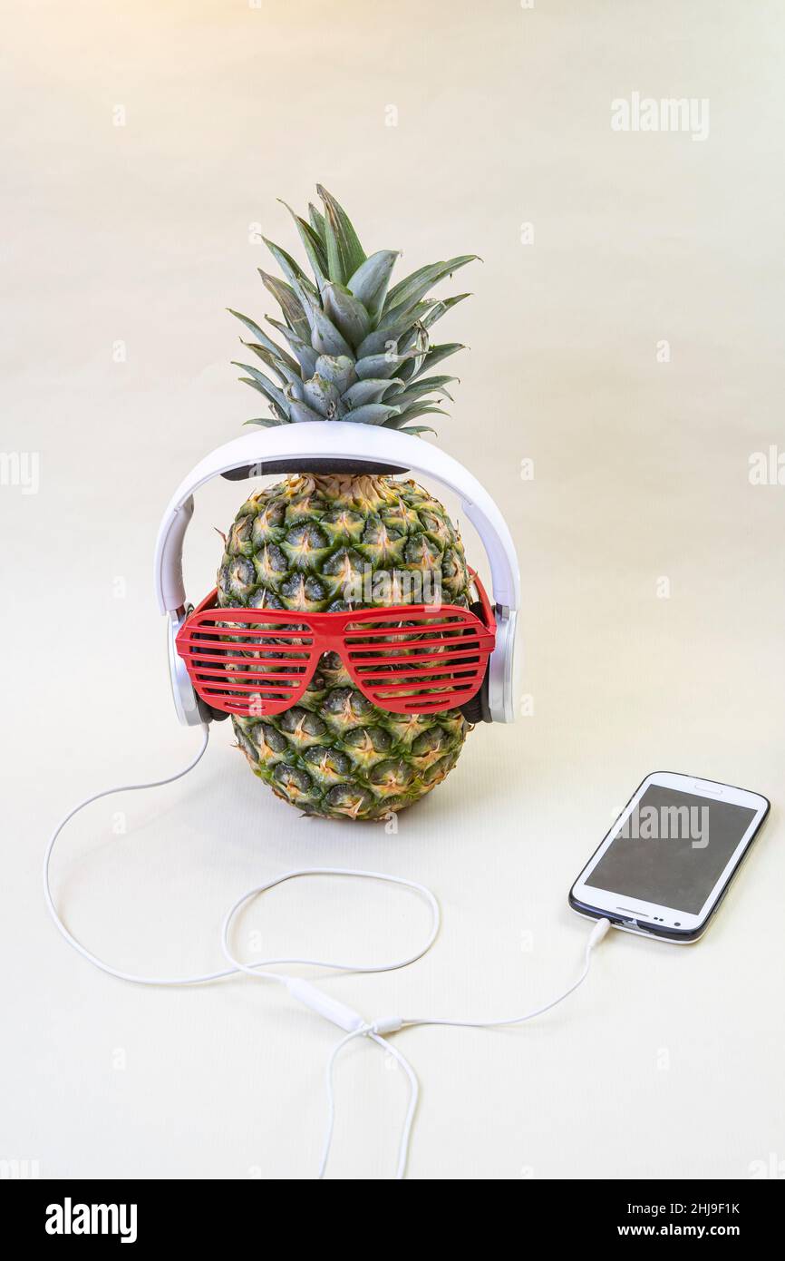 Ananas con bicchieri da discoteca, cuffie bianche e smartphone. Concetto di festa tropicale. Foto Stock