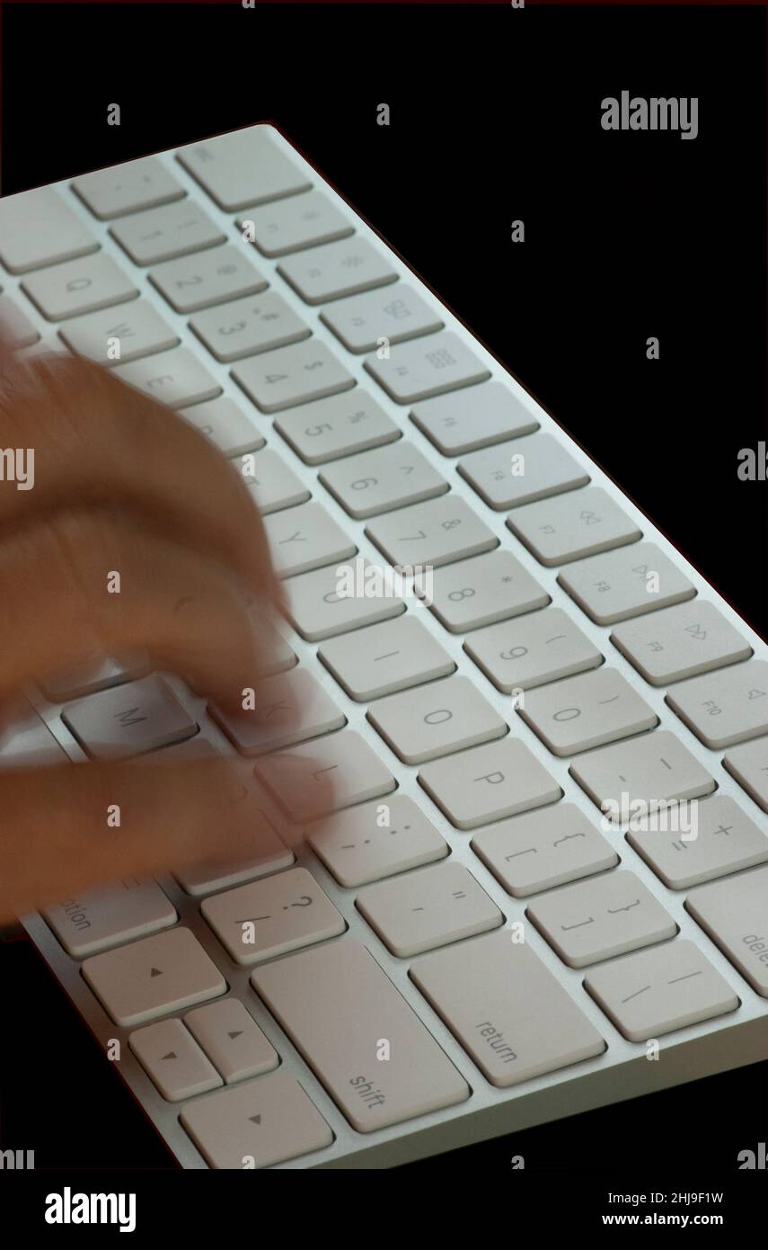 Dita sfocate che lavorano velocemente su tastiera bianca e argentata. Primo piano con sfondo nero e spazio di testo. Foto Stock