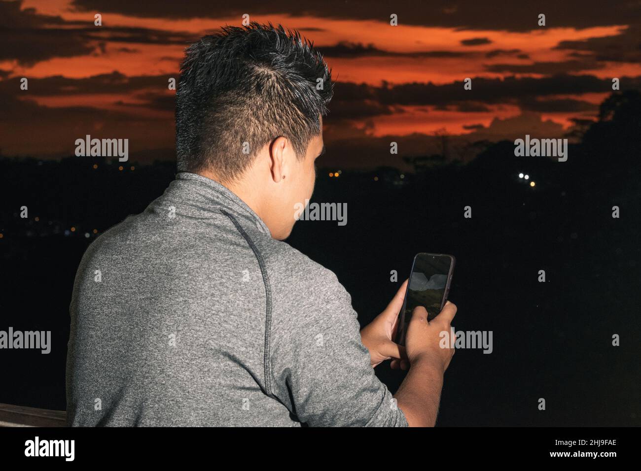 Giovane ragazzo latino bruno-skinned, guardando i suoi social network, sullo sfondo un bellissimo tramonto in Colombia-Pereira, studente che prende una foto per Foto Stock