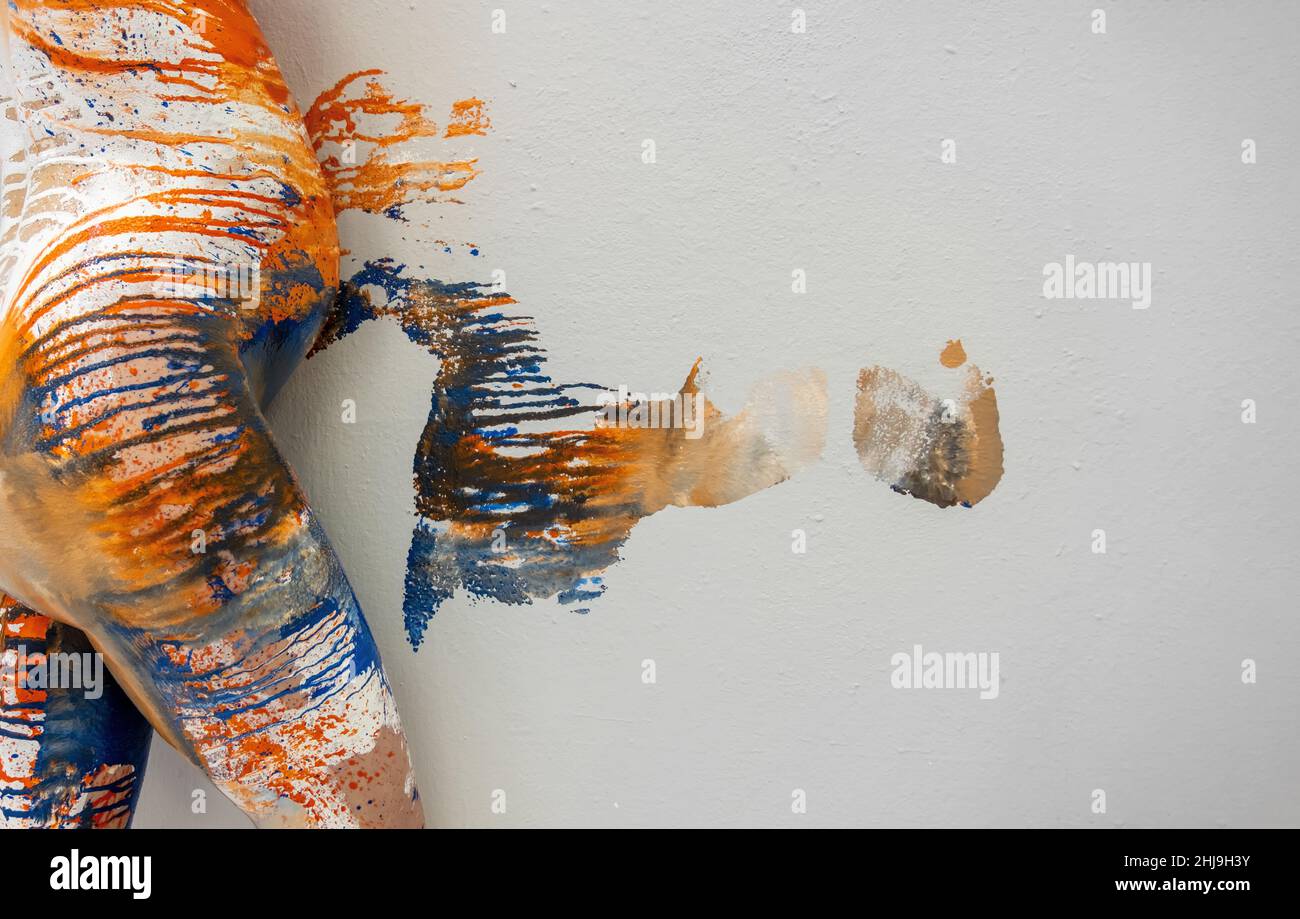 Giovane donna incinta dipinta artisticamente astratta con pittura arancione, blu, bianca, rotola la sua grande ventre rotonda sulla parete dello studio, lasciando il col artistico Foto Stock