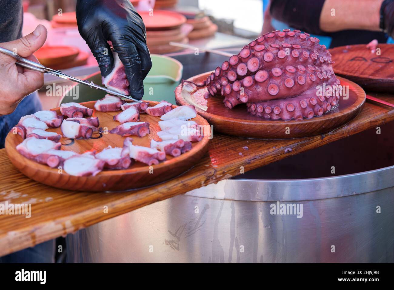 Uomo irriconoscibile che taglia il polpo di stile galiziano e lo mette su lastre di legno. Foto Stock