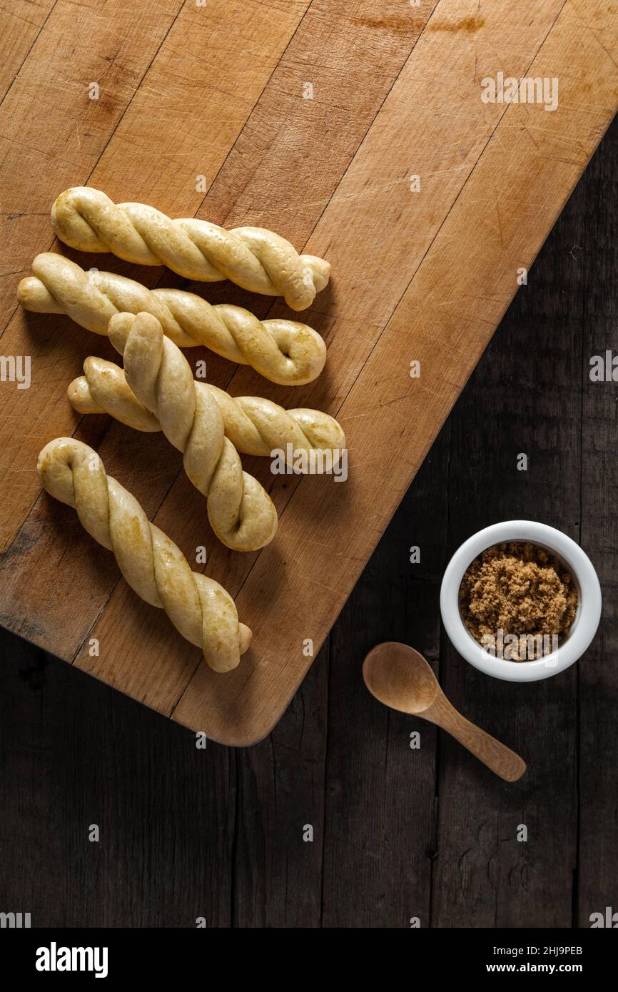 Una colazione a base di bastoncino di pane al forno si gira con una tazza di zucchero di canna posta su un tavolo di legno nero. Foto Stock