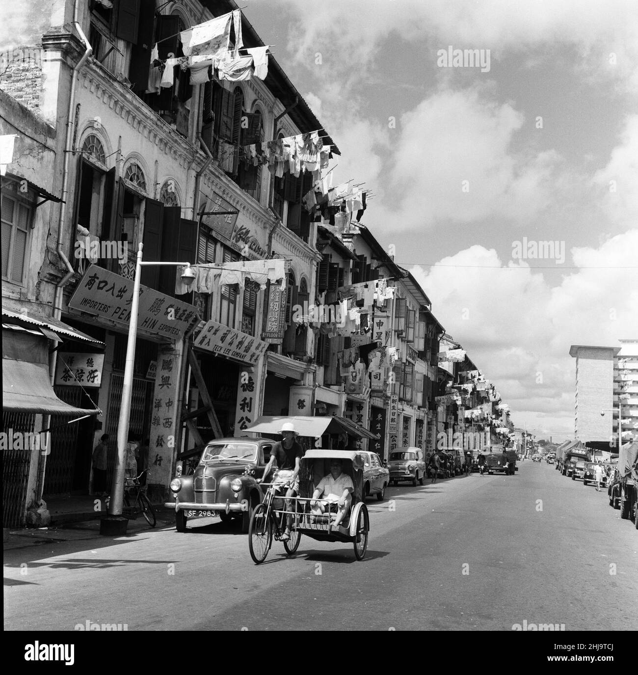 Scene a Chinatown, Singapore. Upper Hokien Street, dove il vecchio incontra il nuovo. I lavaggi puliti sono spoked fuori dalle finestre da entrambi gli edifici vecchi e nuovi mentre le limousine o i trishaws eleganti fanno il loro senso durante il calore di mattina. 6th febbraio 1962. Foto Stock