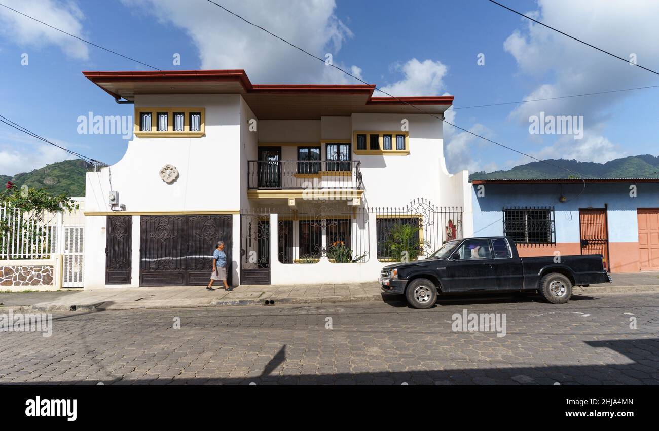 La donna cammina vicino a una casa del medico con le colline sullo sfondo a Jinotega, Nicaragua Foto Stock