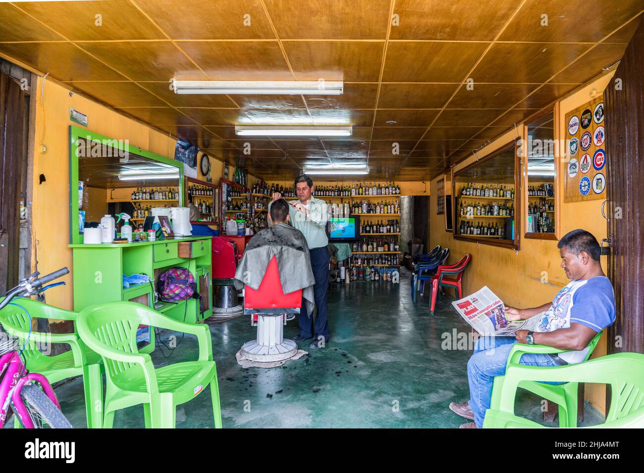 Il barbiere taglia i capelli di un uomo mentre un altro legge un giornale in un negozio di barbiere a Jinotega, Nicaragua Foto Stock