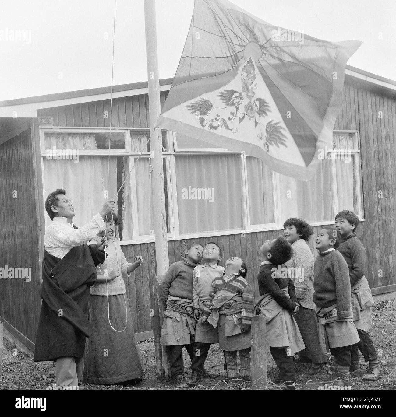 Bambini rifugiati tibetani al Villaggio Pestalozzi per Bambini a Sedlescombe, Sussex orientale, 7th marzo 1963. La nostra immagine mostra ... ogni mattina, la bandiera tibetana è gestito nella loro modesta casa. I tredici ragazzi e le otto ragazze arrivarono nel Regno Unito, da un campo profughi nel nord dell’India. Molti ora orfani, i bambini sono fuggiti dall'occupazione e dalla persecuzione cinesi. La comunità prende il nome dall'educatore svizzero del XVIII secolo, Johann Heinrich Pestalozzi, che ha dedicato la sua vita alla chiusura delle divisioni nella società attraverso l'educazione dell'intera persona, del suo capo, del suo cuore e delle sue mani. Foto Stock