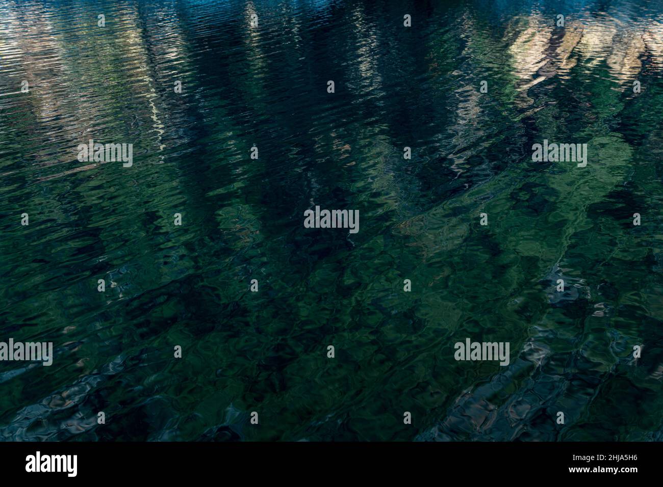 superficie ondulata di acqua trasparente di un lago puro con riflessi di montagne e legno Foto Stock