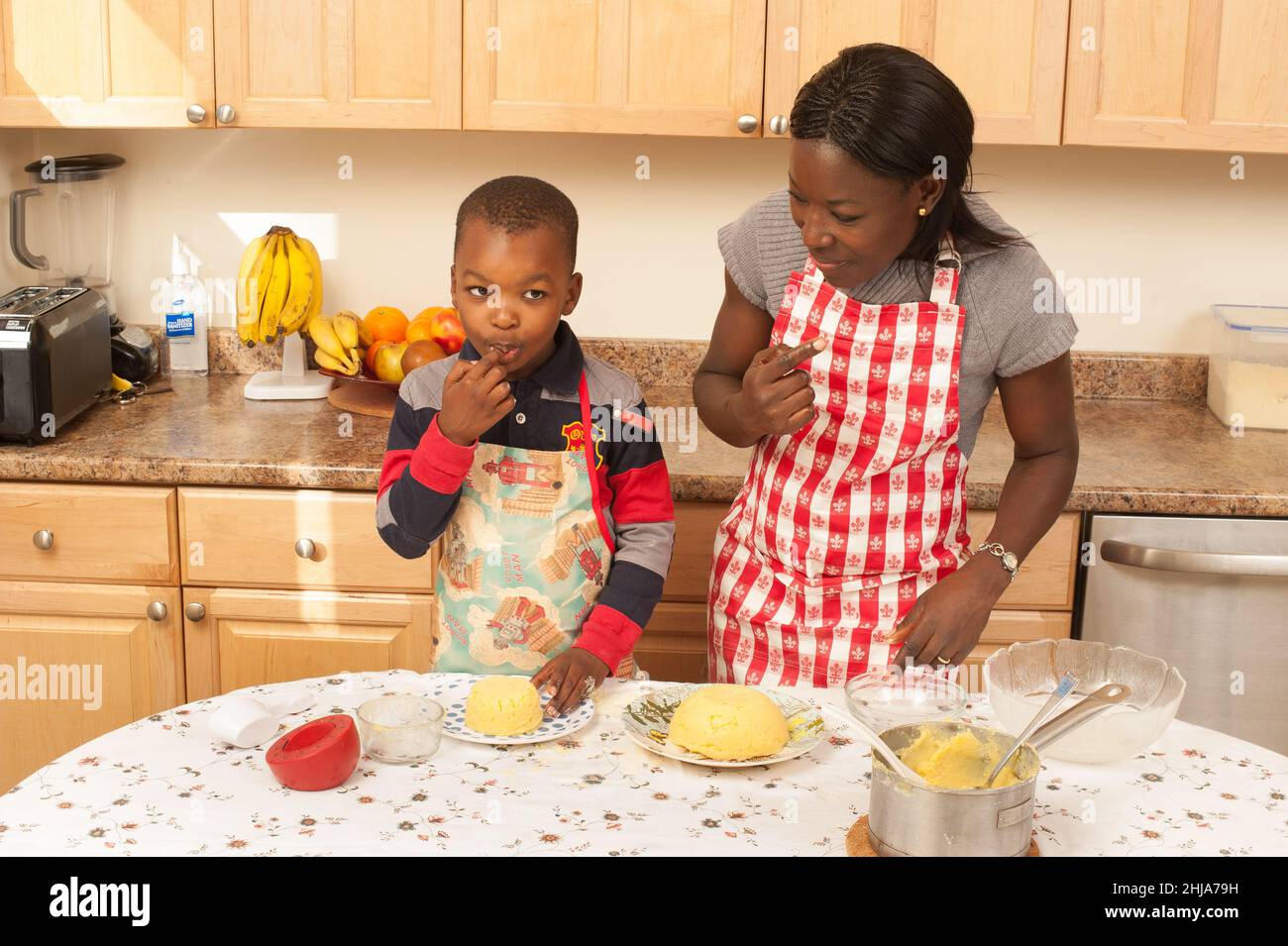 Ragazzo di 4 anni in cucina a casa con sua madre dopo piatto togalese fatto con farina di mais 'fufu', felice, dandogli un gusto Foto Stock