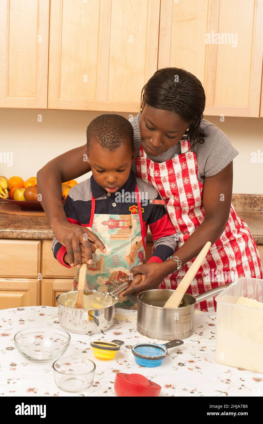 Ragazzo di 4 anni in cucina a casa con sua madre mescolando togalese piatto fatto con farina di mais 'fufu' Foto Stock