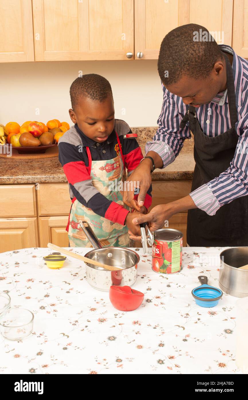 ragazzo di 4 anni in cucina con il padre imparando come usare il apriscatola per aprire lattina di pomodori Foto Stock