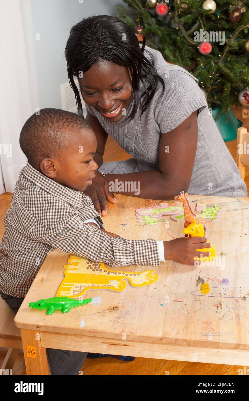 ragazzo di 2 anni che gioca con giocattoli giraffa di diverse dimensioni con puzzle di cartone giraffa davanti a lui, incoraggiato dalla madre Foto Stock