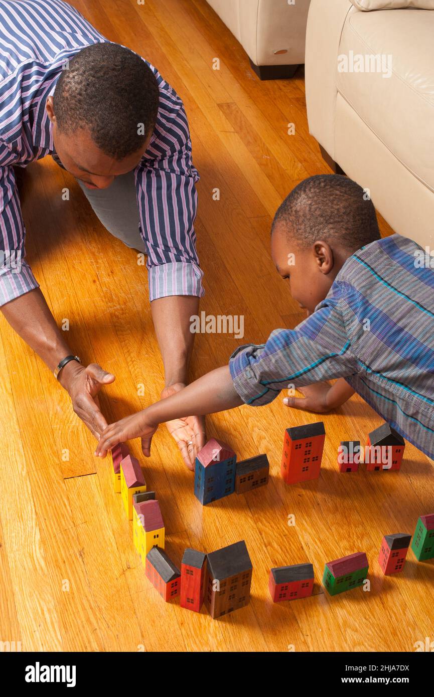 ragazzo di 4 anni che gioca con blocchi di legno e veicoli costruire città o strada con l'aiuto del padre Foto Stock