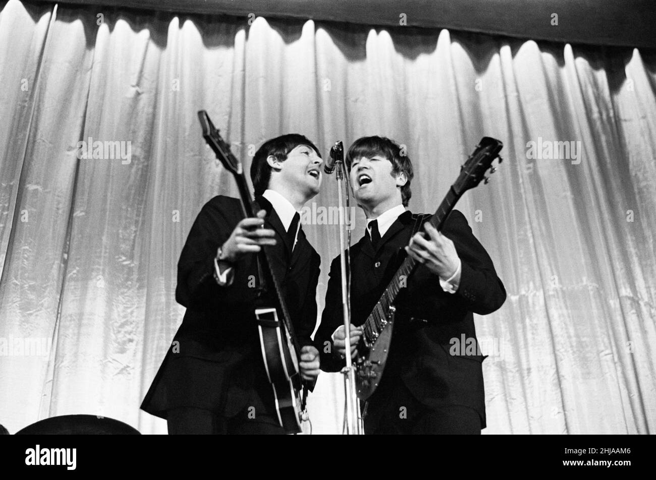 Paul McCartney e John Lennon condividono il microfono durante una performance del gruppo pop britannico The Beatles. Novembre 1964. Foto Stock
