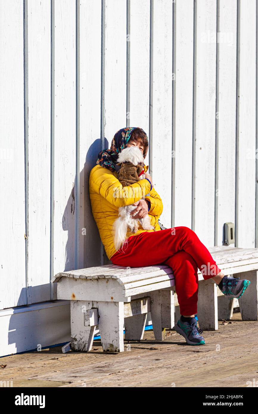 Donna vestita con il suo cane seduto al sole lungo il lungomare di Steveston in British Columbia Canada Foto Stock