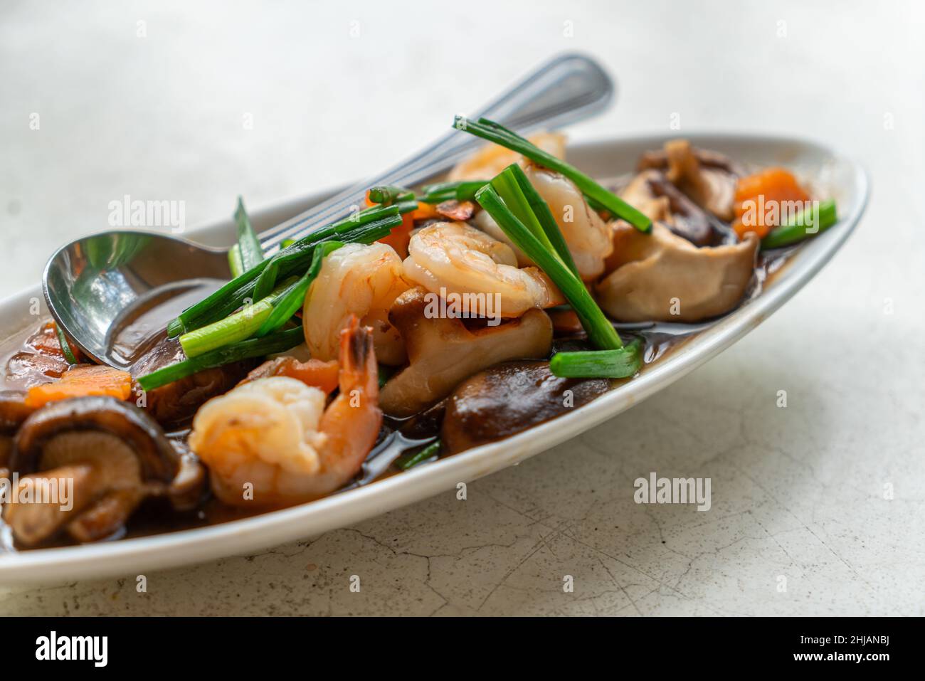 Gamberetti fritti, funghi Shiitake o funghi cinesi con salsa di ostriche in un bellissimo piatto ovale sul tavolo in pietra bianca, immagine ravvicinata Foto Stock