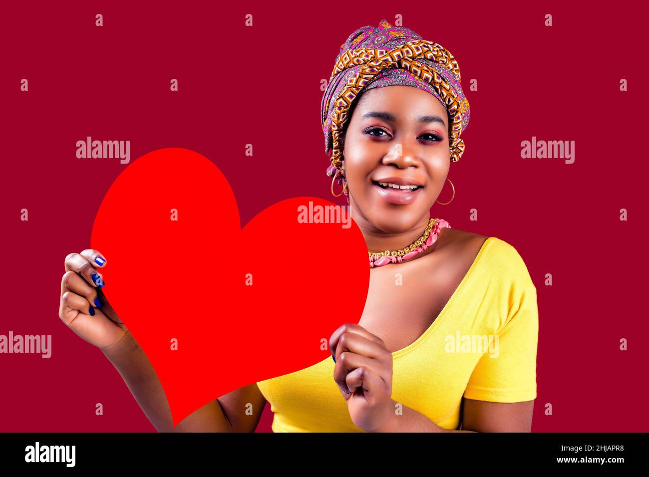 attraente bella donna sud con turbante tenuta in mani cuore isolato su sfondo rosso san valentino giorno 14 febbraio Foto Stock