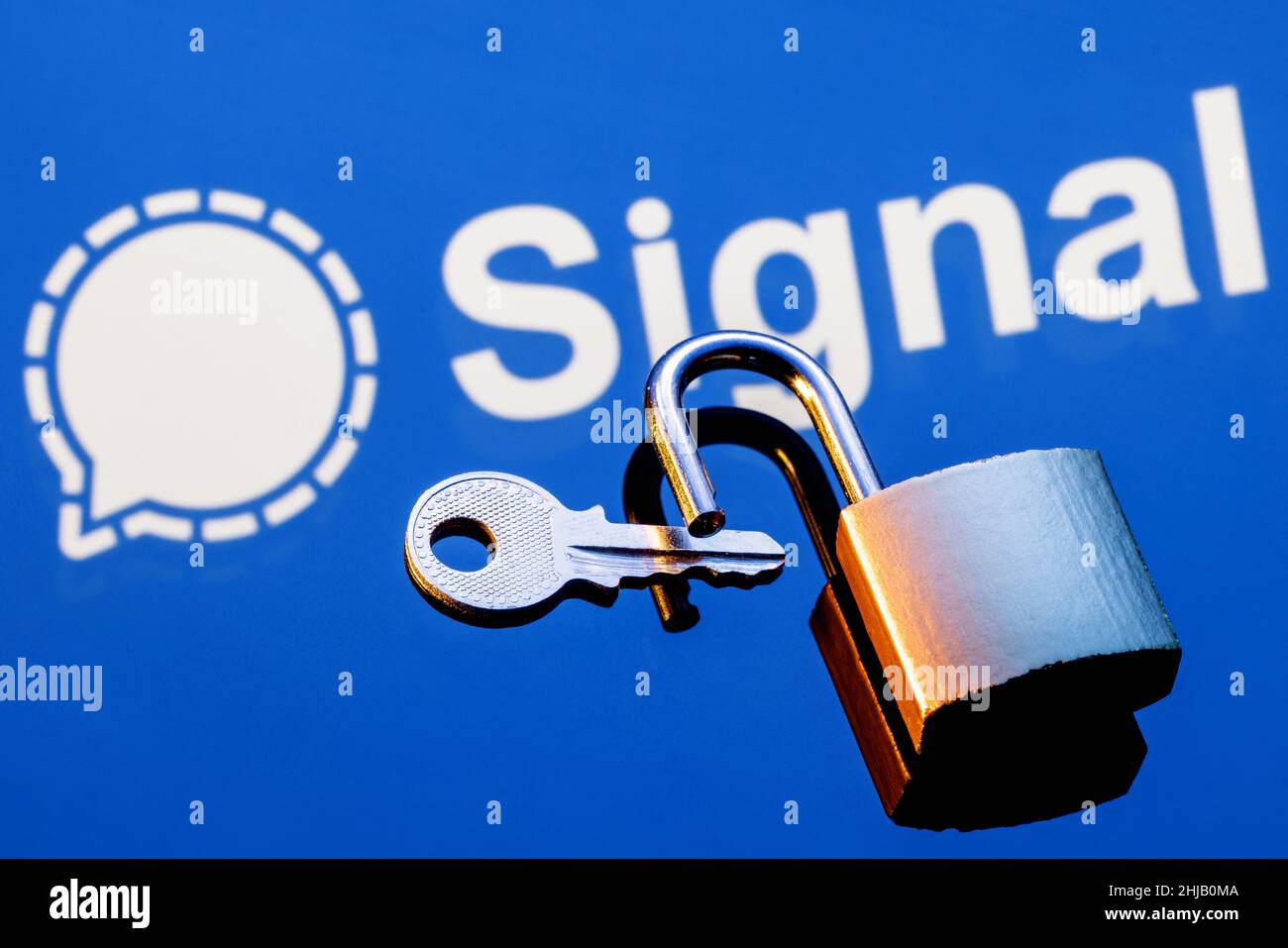 Un lucchetto di sicurezza aperto e una chiave sullo sfondo del logo del servizio di messaggistica istantanea con crittografia del segnale nella riflessione del mirror. Foto Stock