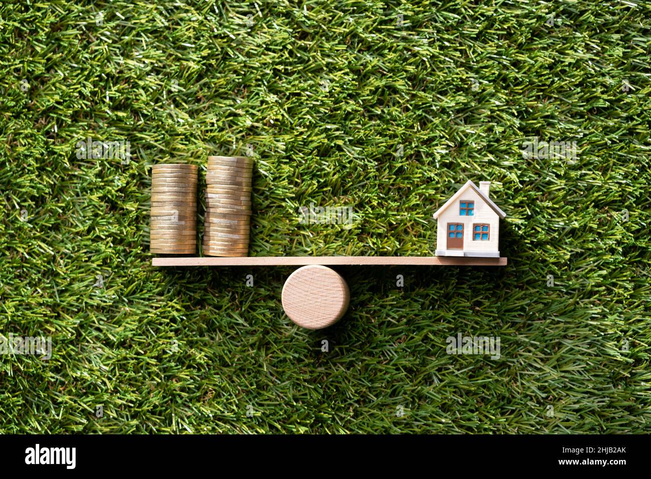 Primo piano della casa modello e monete in equilibrio su legno scala di pesatura Foto Stock