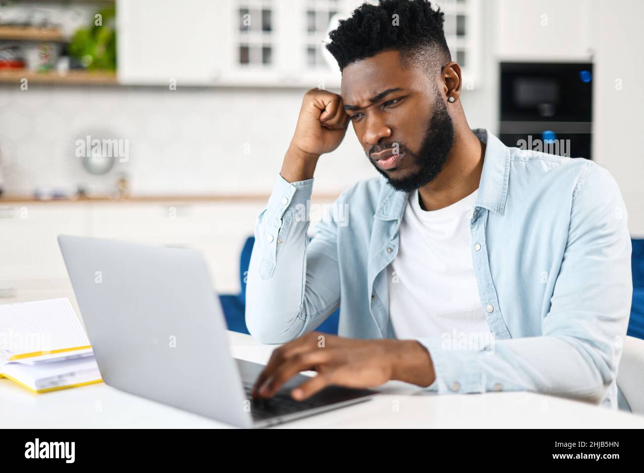 Multi-razziale maschio freelance o studente seduto sul divano, sensazione di stanchezza per il lavoro costante sul computer, toccare tempio, avere un mal di testa e non può concentrarsi Foto Stock