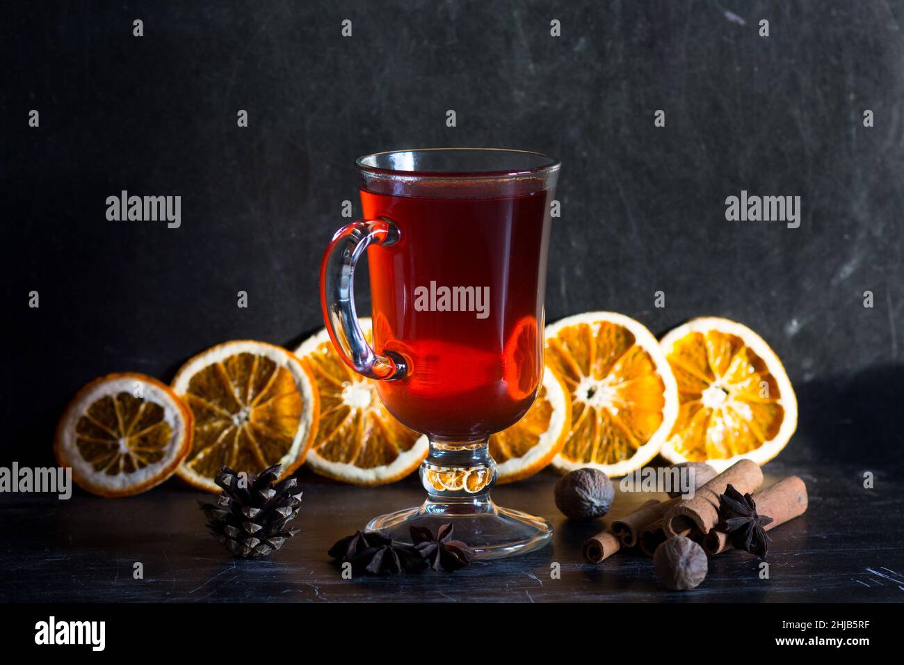 Bicchiere di VIN brulé, spezie e pezzi di arance su sfondo nero Foto Stock