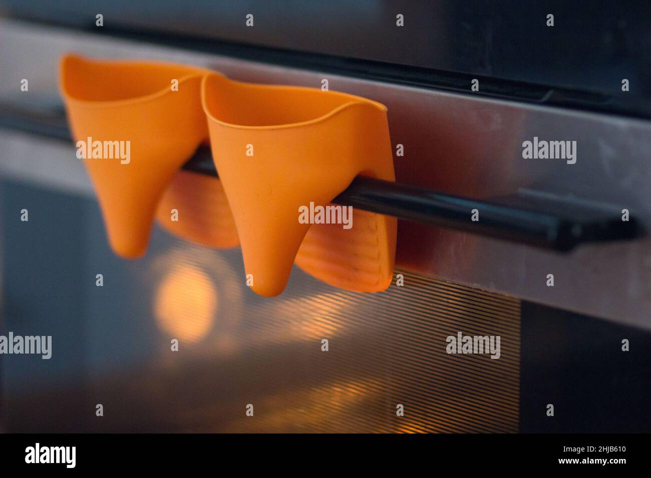 Guanti resistenti al calore arancioni appesi sullo sportello del forno Foto Stock