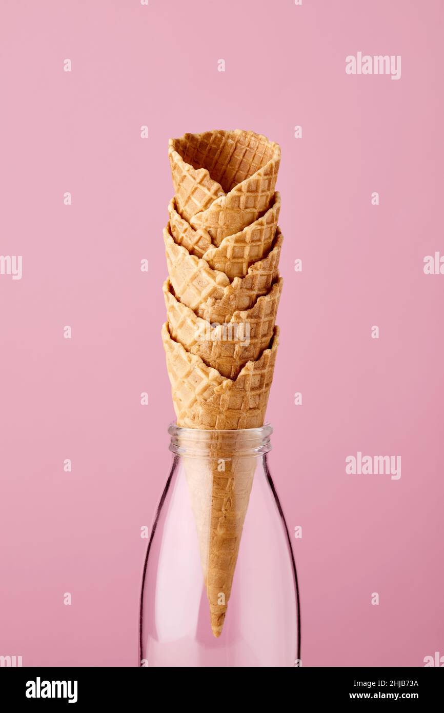Svuotare i coni del gelato in una bottiglia di latte di vetro su sfondo rosa pastello. Foto Stock
