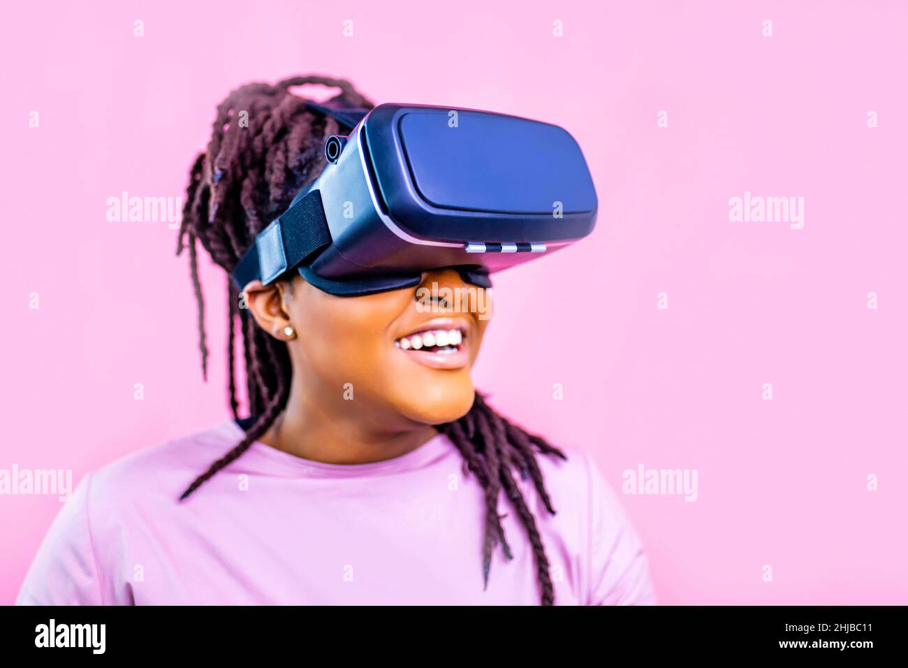 donna etnica nera che guarda la simulazione della vita video su sfondo rosa dello studio Foto Stock