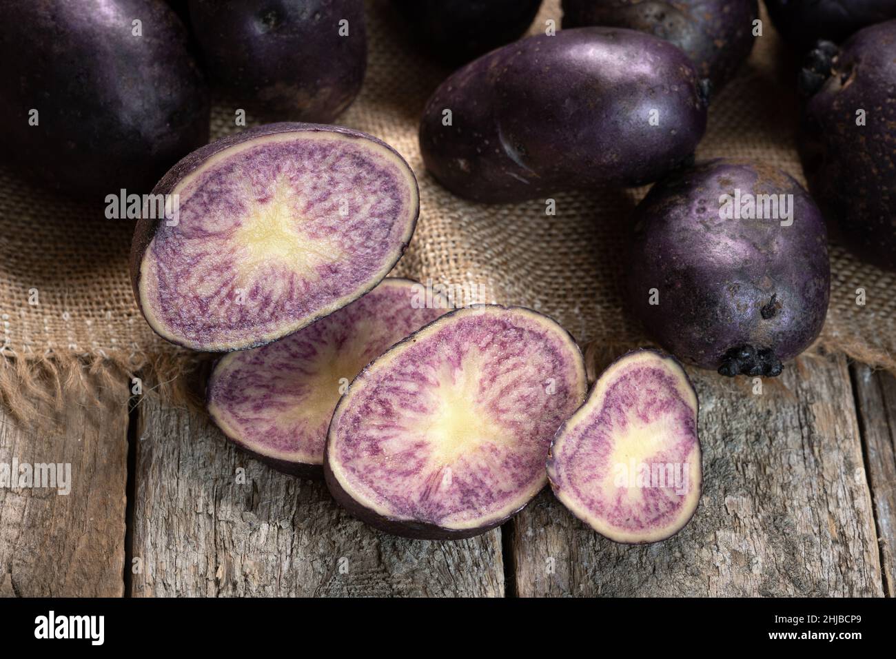 Patate viola vitelotte tagliate a fette sulle tavole di legno e sul panno  di burlap Foto stock - Alamy