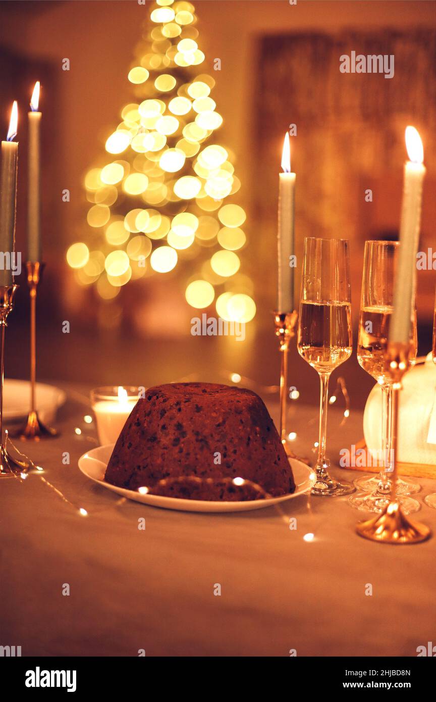 Accogliente foto del tavolo da pranzo con torta di Natale appena sfornata, candele brucianti, luci di Natale come decorazione e bicchieri alti riempiti di champagne ag Foto Stock