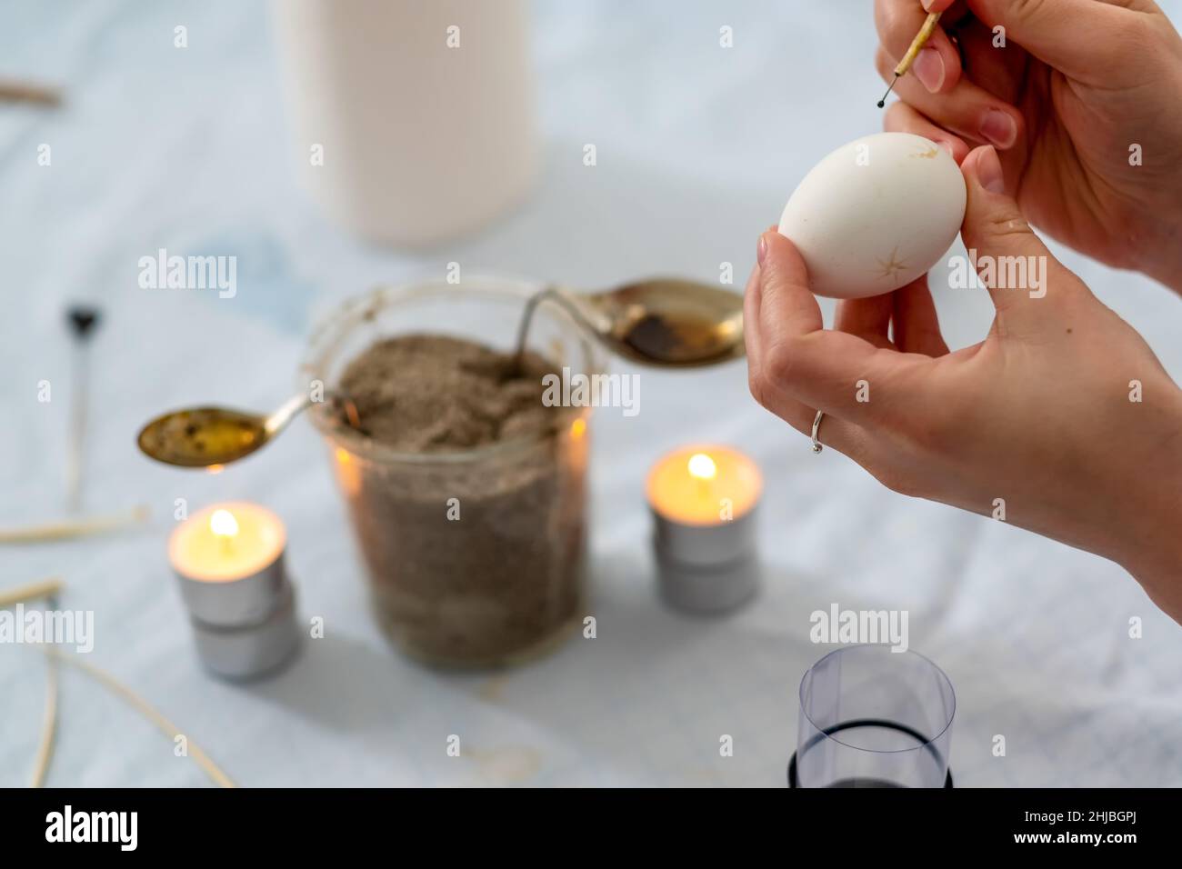 Le mani femminili dipingono un uovo di Pasqua bianco secondo la tradizione tedesca sorbiana con una testa dell'ago e le api fuse e la cera della candela della luce del tè, spazio di copia Foto Stock