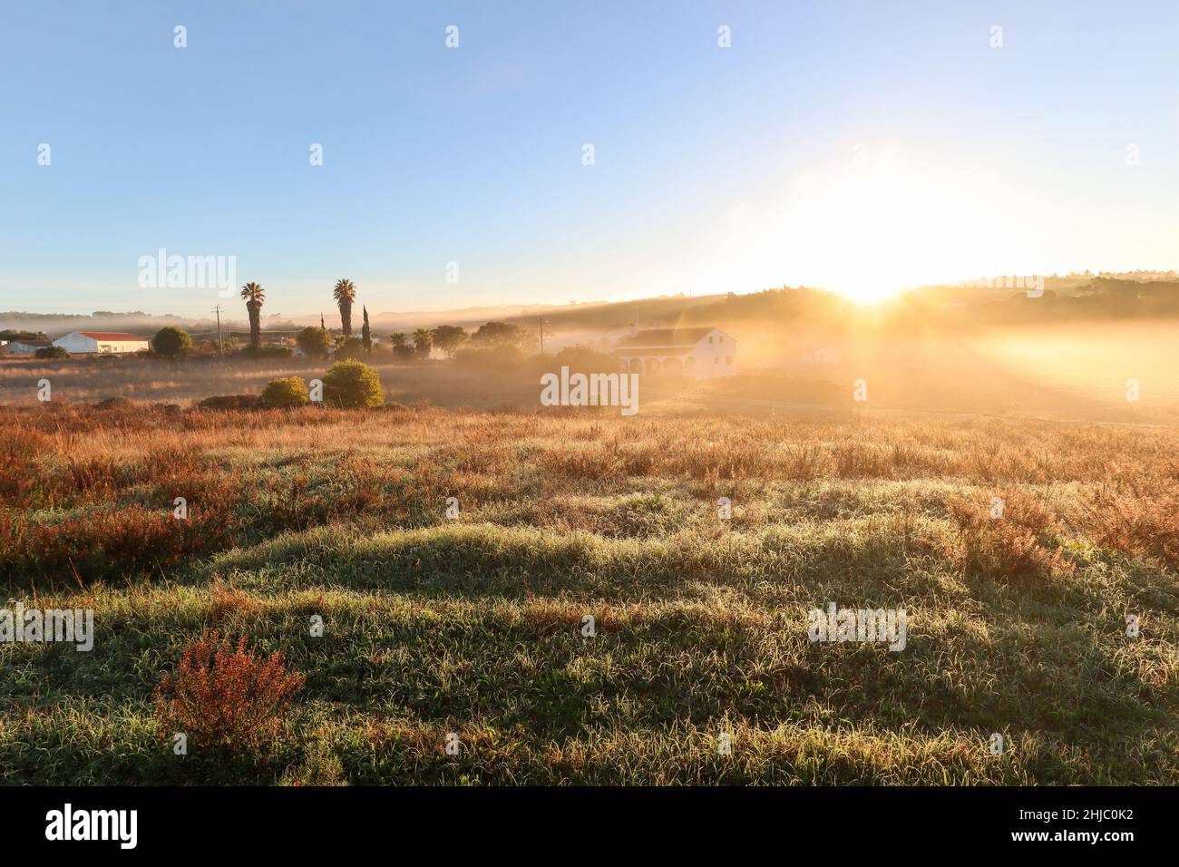 Vista sul paesaggio tipico dell'Alentejo con villaggio portoghese al mattino nebbia un sole che sorge sul sentiero escursionistico Rota Vicentina vicino a Carrascalinho, Aljezur Foto Stock
