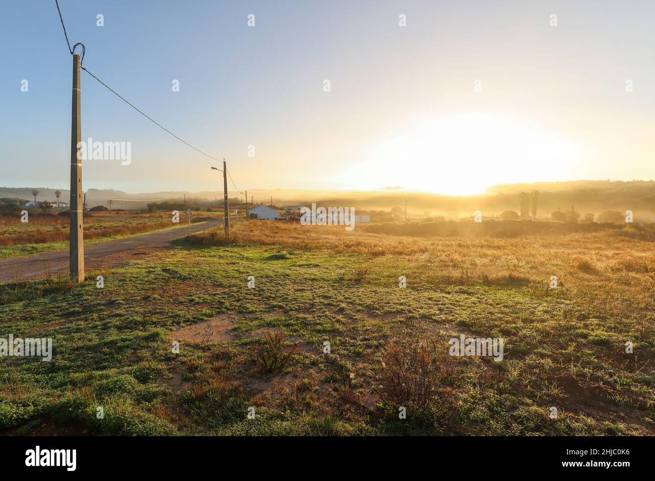 Vista sul paesaggio tipico dell'Alentejo con villaggio portoghese al mattino nebbia un sole che sorge sul sentiero escursionistico Rota Vicentina vicino a Carrascalinho, Aljezur Foto Stock