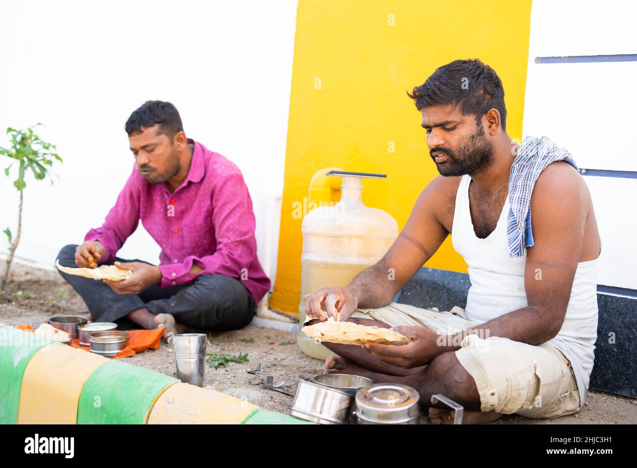 Il lavoratore di costruzione indiano occupato avere pranzo di pomeriggio sul posto di lavoro - concetto di igiene, sanità, tempo di pausa e stile di vita quotidiana delle scommesse Foto Stock
