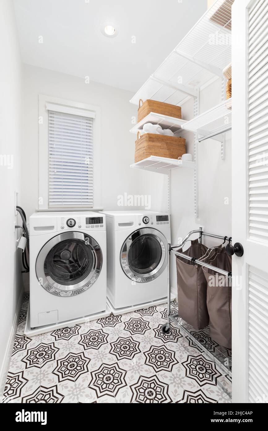 Una lavanderia con lavatrice e asciugatrice bianca, pavimento in piastrelle a motivi geometrici e scaffalature organizzate sulla parete. Foto Stock