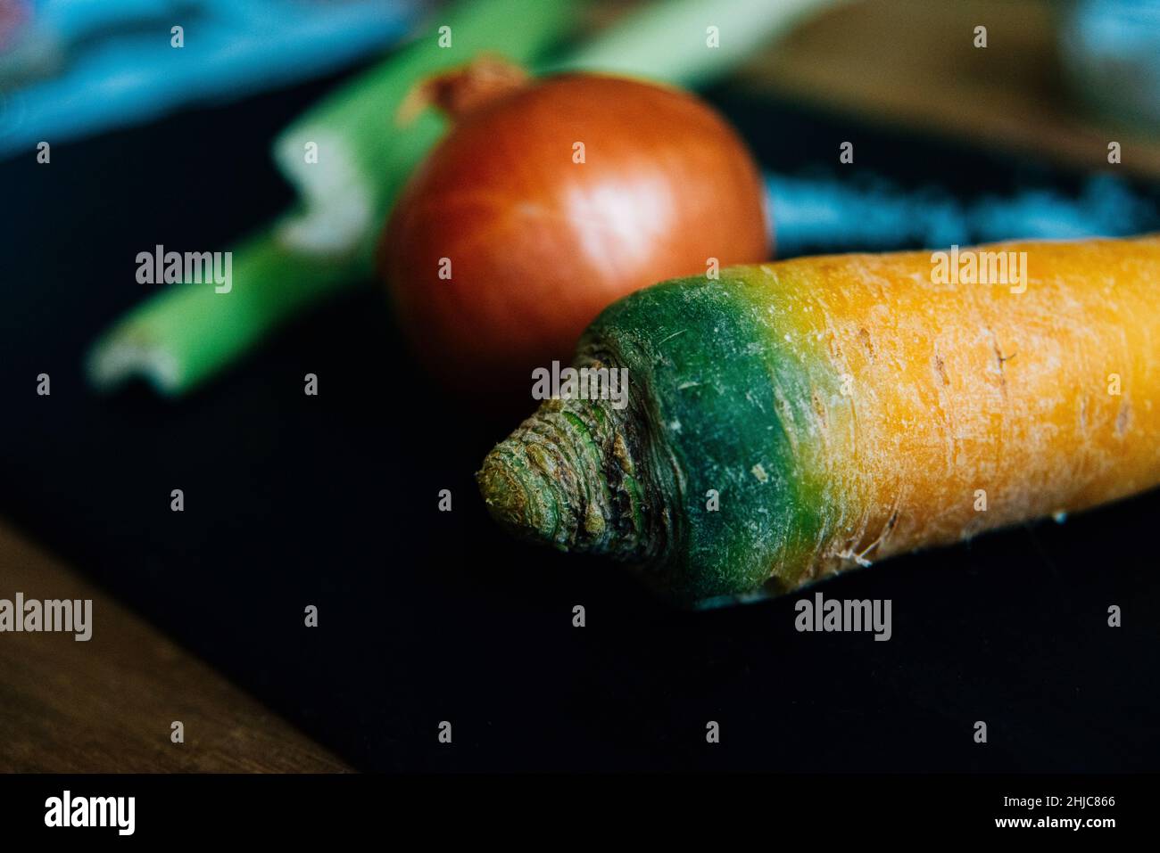 Primo piano di una carota con una cipolla e sedano sfocati sullo sfondo su ardesia grigia. Ingredienti per base di cottura mirepoix francese. bol. SPAG Foto Stock