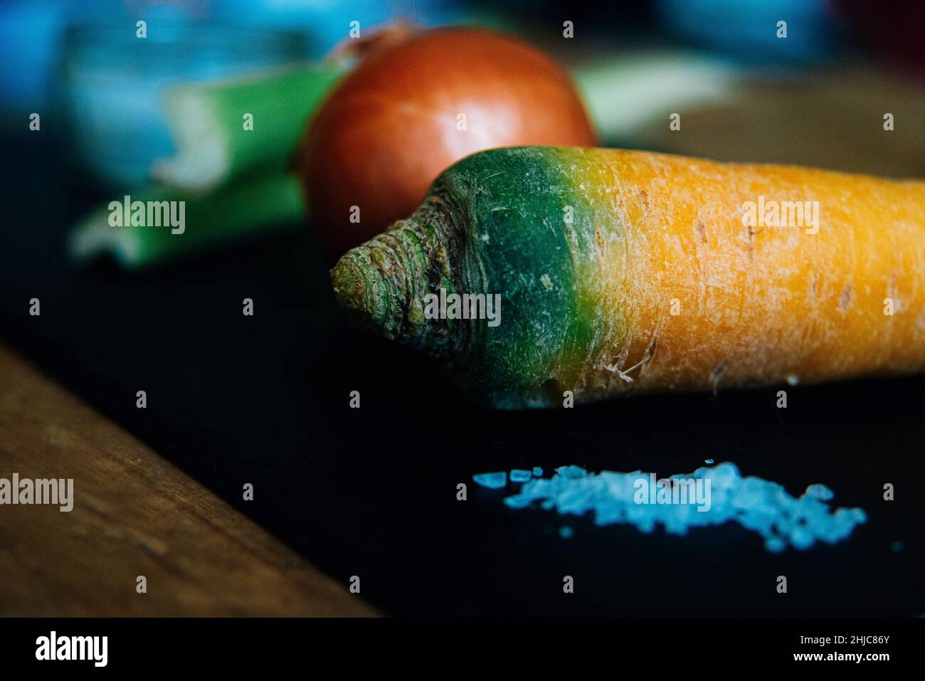 Primo piano della carota, con cipolla e sedano sfocati sullo sfondo, su un piano di lavoro da cucina pronto per essere preparato. Ingredienti base mirepoix tradizionali Foto Stock