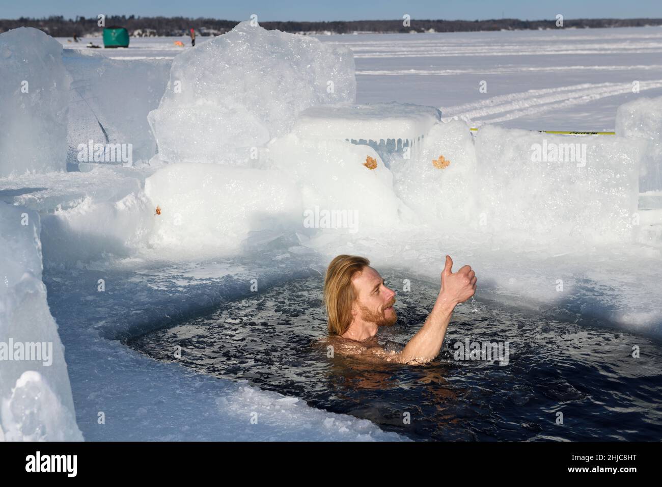 Uomo che dà i pollici in su nel sole che nuota in una buca di ghiaccio per una nuotata di acqua fredda in inverno a Kempenfelt Bay Lago Simcoe Barrie Ontario Foto Stock