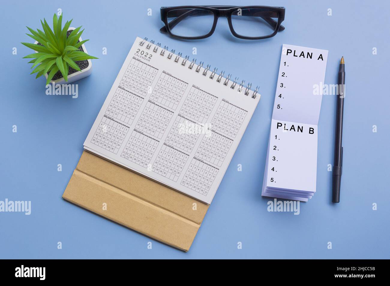 Testo su blocco note con calendario 2022, bicchieri, penna e piante in vaso su una scrivania - piano A, piano B. Foto Stock