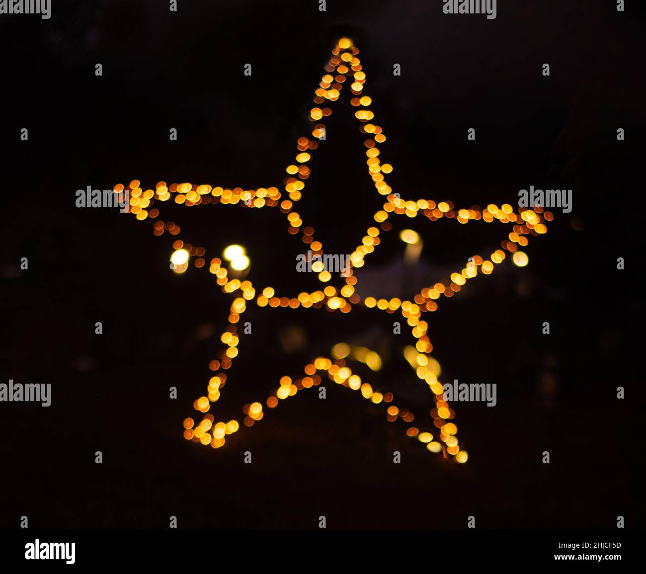 una stella sfocata da bokeh di luci. ornamento in oro a forma di stella su sfondo nero. Sfondo sfocato di Natale Foto Stock