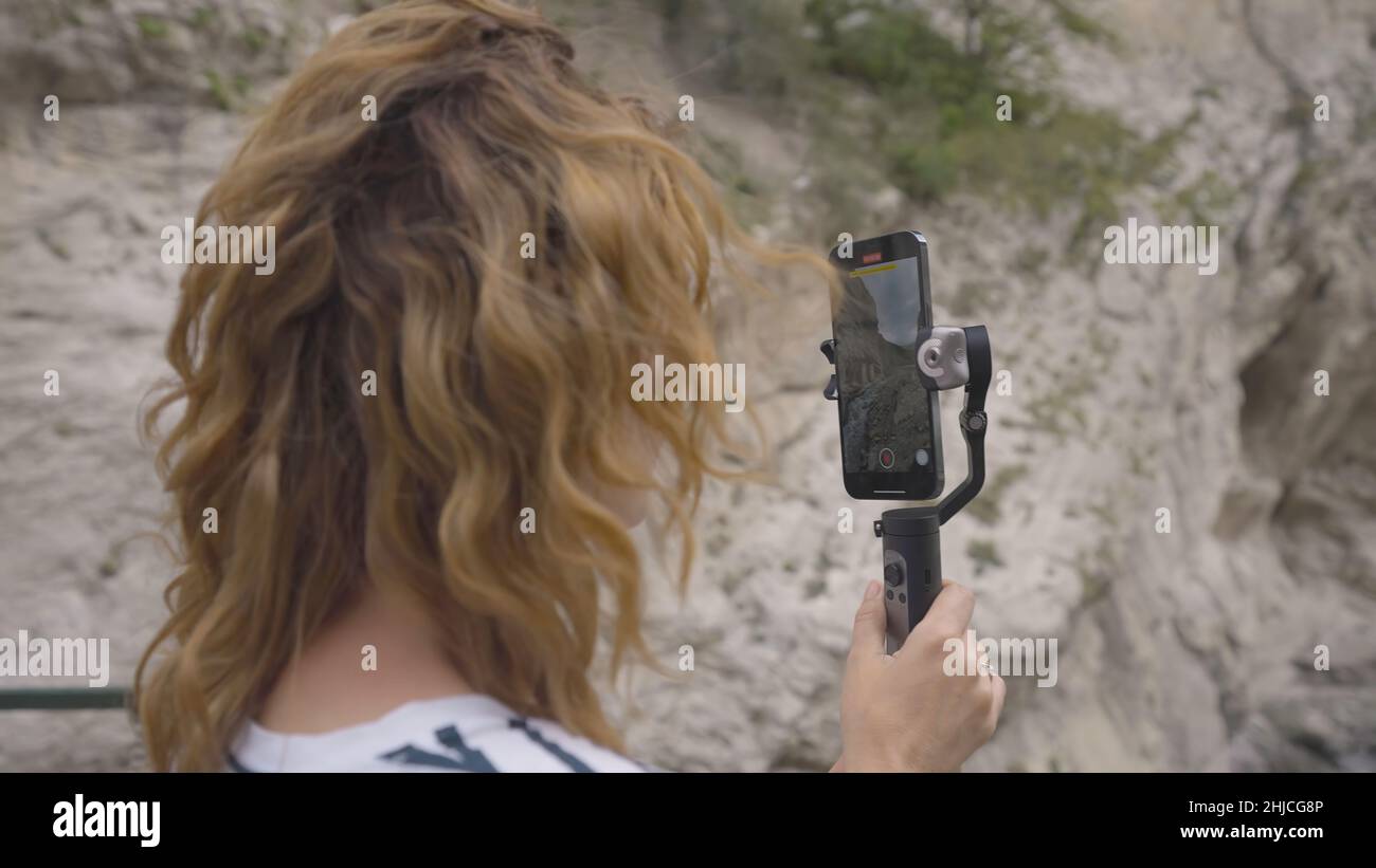 Bella donna scatta foto al telefono con salda. Azione. Giovane donna scatta foto al telefono con stabilizzatore manuale. Il viaggiatore scatta foto Foto Stock