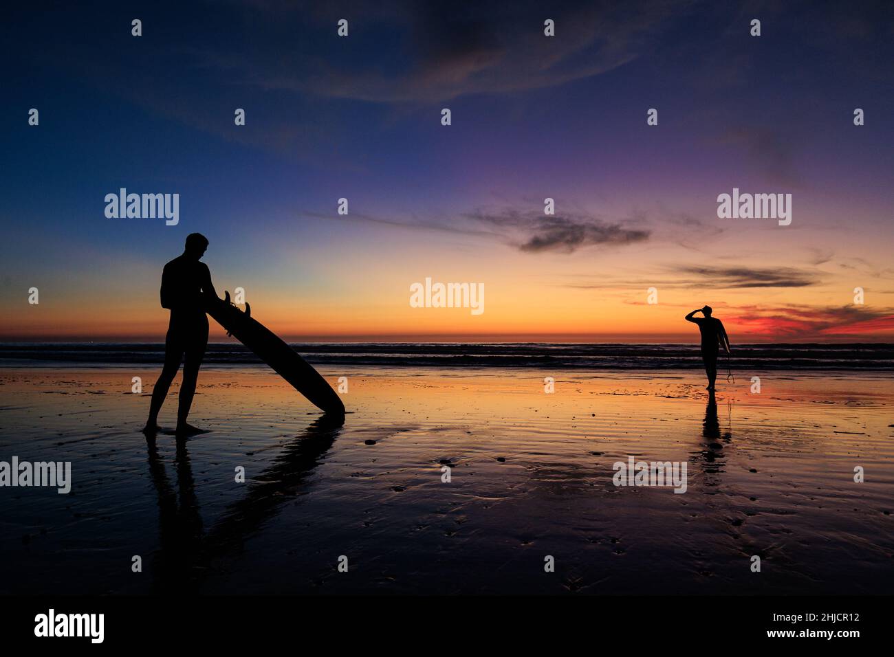 I surfisti su una spiaggia lucida con bassa marea guardano un colorato tramonto invernale dopo il surf a Torrey Pines, San Diego, California. Foto Stock