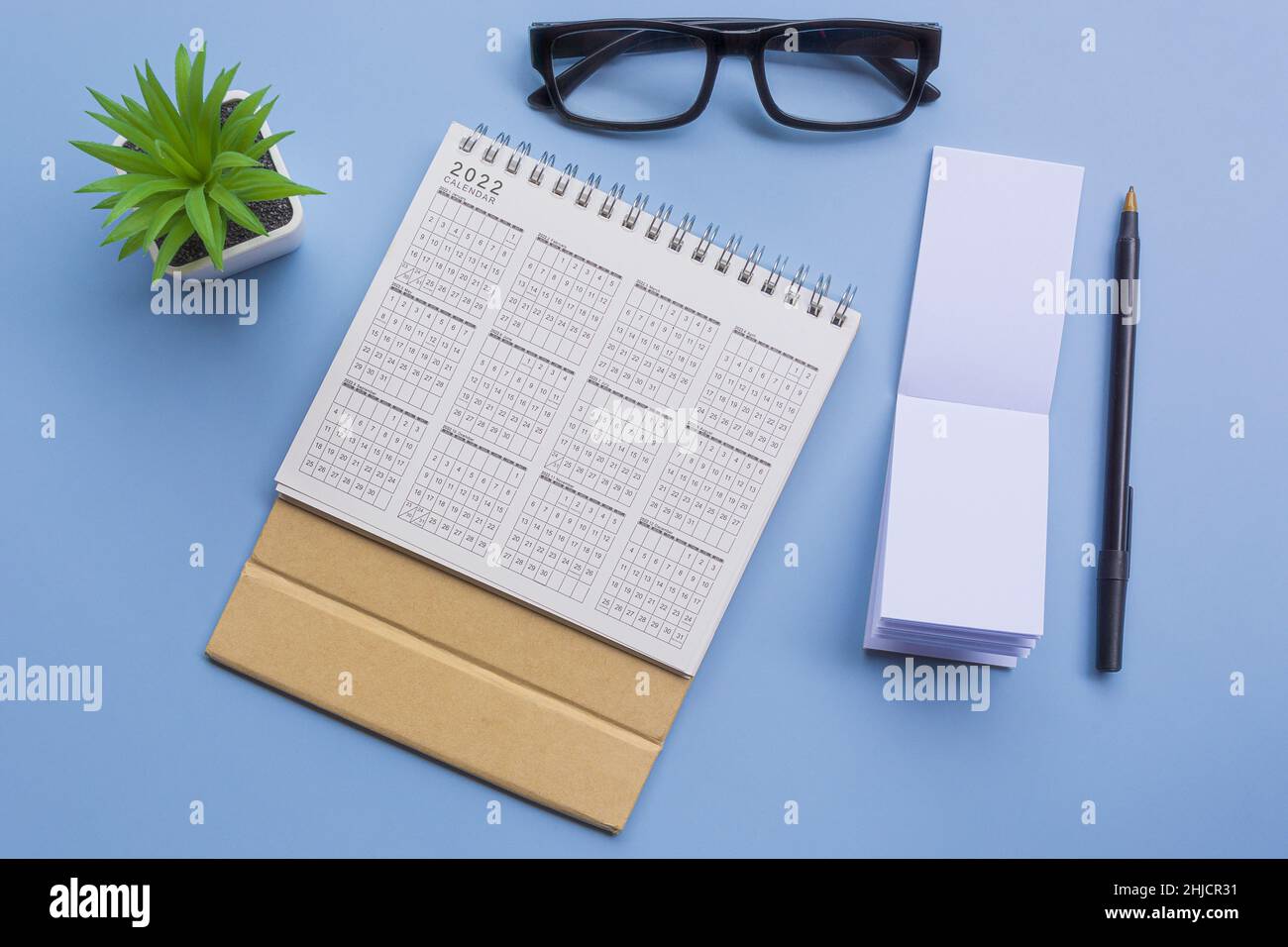Blocco note con 2022 calendario, bicchieri, penna e piante in vaso su una scrivania. Disposizione piatta Foto Stock